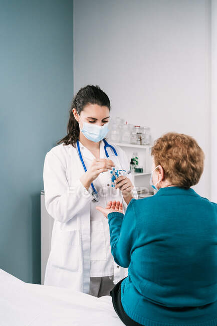 Ärztin in Uniform und Einmalmaske bereitet Medikamente für anonyme ältere Patientin auf Konsultation in der Klinik während der Pandemie vor — Stockfoto