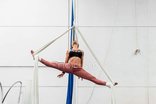 Полное тело спортивной подвижной неузнаваемой женщины в активной одежде, выполняющей расщепления на воздушных шелков во время тренировок в гимнастической студии — стоковое фото