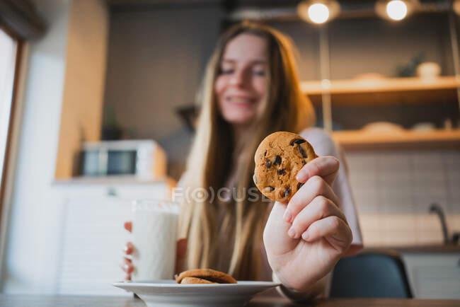 Jovem alegre com saboroso biscoito de aveia com chips de chocolate para café da manhã na mesa na cozinha — Fotografia de Stock