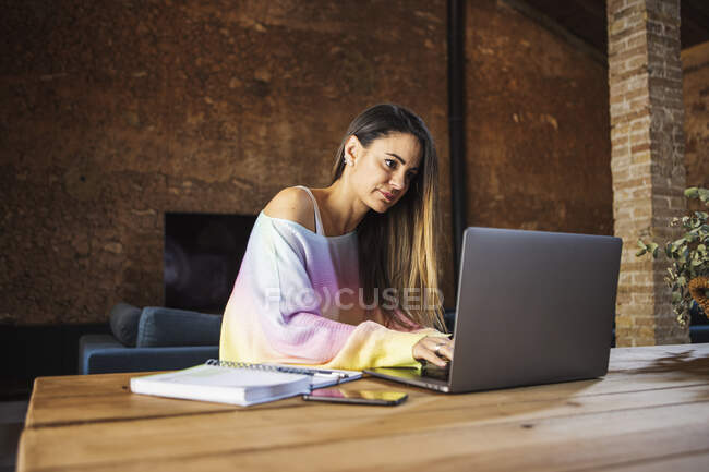 Content female remote employee with cellphone and netbook at table in house — Foto stock