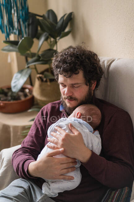 Adult bearded father holding little child while sitting and sleeping in armchair in house room — Stock Photo