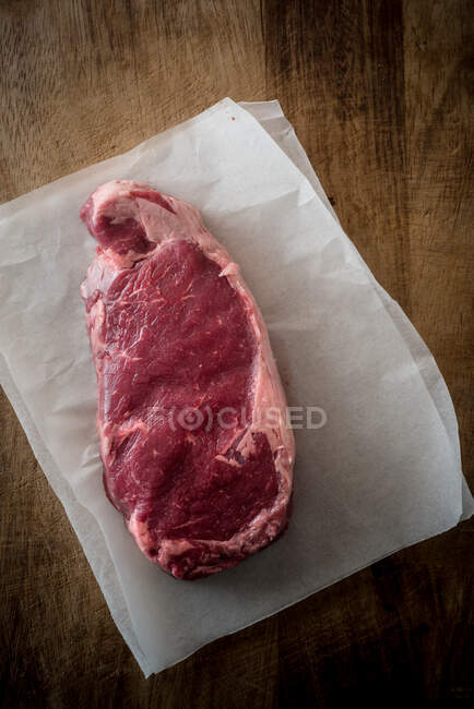 Visão aérea da peça de carne não cozida com folhas de alecrim contra papel manteiga no fundo marrom — Fotografia de Stock