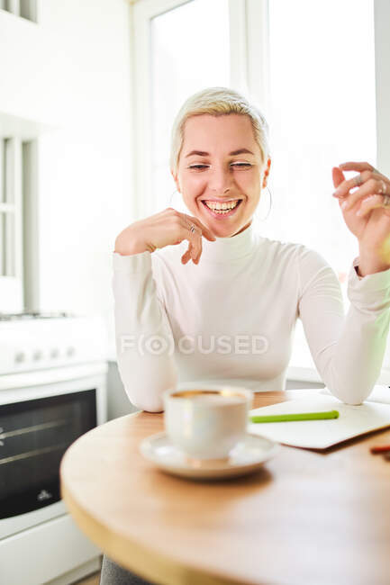 Happy female astrologist drinking hot beverage from cup while looking down at home in sunlight — Stock Photo