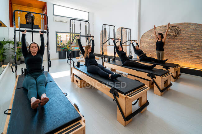 Company of females in sportswear stretching body on pilates reformers during training under supervision of professional instructor — Stock Photo