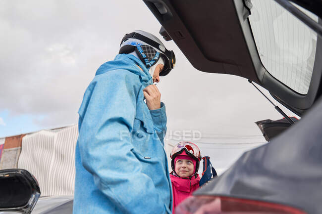 Вид сбоку отец и дочь в теплой спортивной одежде и размещение лыж в багажнике автомобиля в солнечный зимний день — стоковое фото