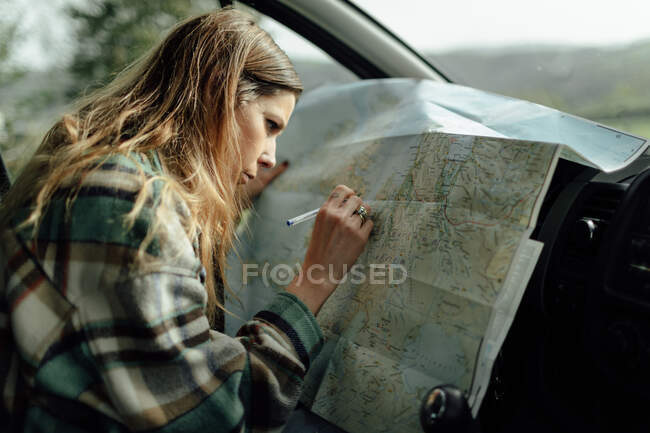 Вид сфокусированной туристки, делающей заметки на карте маршрута, сидя в машине — стоковое фото