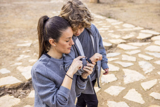 Von oben erwachsene Mutter in Freizeitkleidung zeigt auf Armbanduhr an der Hand des Jungen, während sie auf holprigem Gehweg interagiert — Stockfoto