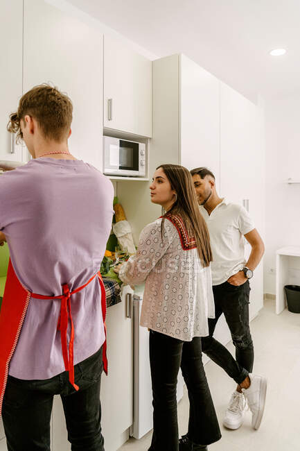 Back view of young multiracial best friends in casual outfits cutting fruits while preparing delicious healthy food in kitchen — Stock Photo