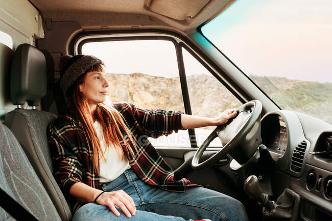 Hipster donna in viaggio seduto sul sedile del conducente in camion parcheggiato in altopiani — Foto stock