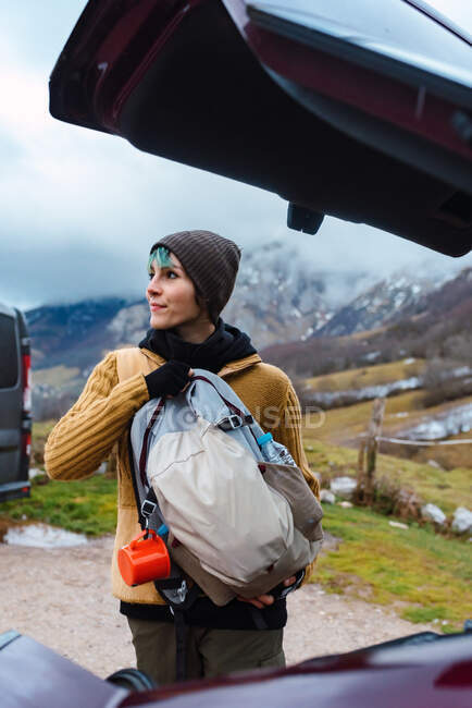 Pensive female packing backpack in car trunk while looking away against mountains of Peaks of Europe in Spain — Stock Photo