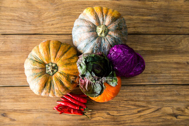 Top view of various pumpkins with red cabbage and red hot chili peppers arranged on wooden table in kitchen — Photo de stock