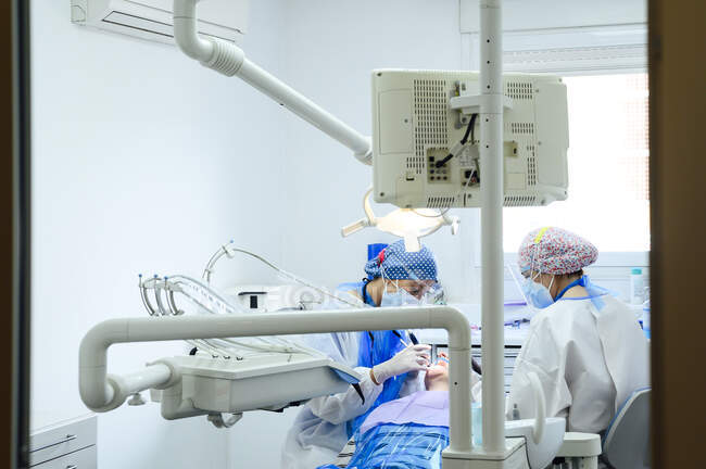 Dentiste anonyme avec un collègue en uniforme opérant les dents du patient à l'aide d'outils médicaux dans une clinique moderne — Photo de stock