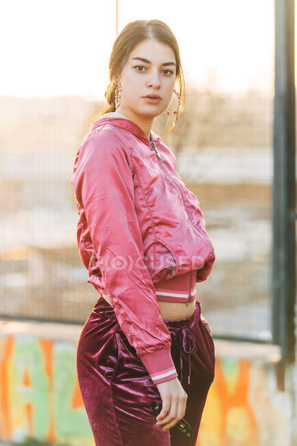Junge Frau in moderner Kleidung und Ohrringen blickt auf verschwommenem Hintergrund in die Kamera in der Stadt — Stockfoto