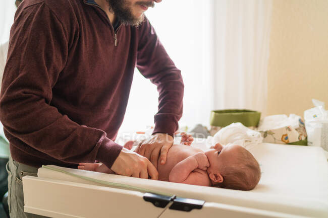 Crop anonymous dad putting diaper on charming little child on infant table in house — Stock Photo