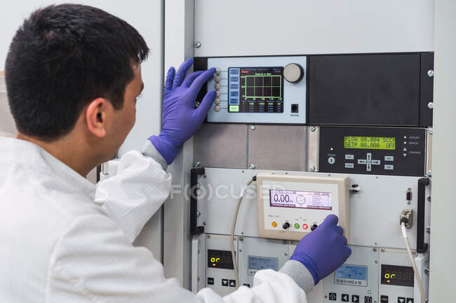 Asistente de laboratorio masculino profesional concentrado en batas blancas y guantes de látex presionando botones en equipos modernos - foto de stock