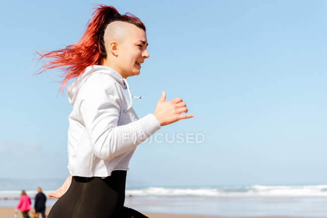 Вид сбоку активной женщины-бегуньи, бегущей по берегу океана во время тренировки летом — стоковое фото