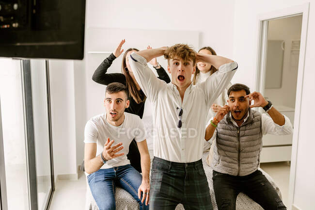Group of expressive young multiethnic friends in casual clothes sitting on comfortable bed and watching sport match together on TV during weekend at home — Foto stock