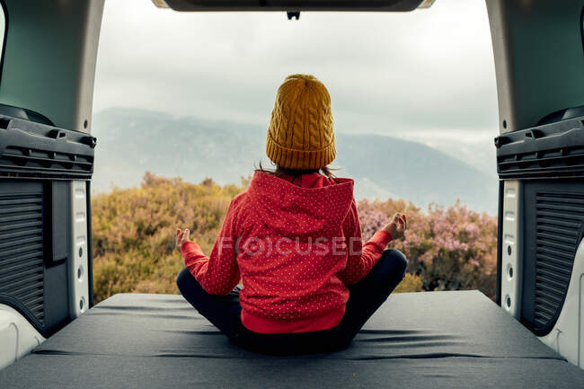Задний вид анонимной девушки-подростка, сидящей в фургоне в позе Лотоса и занимающейся йогой во время медитации во время путешествия в горы — стоковое фото