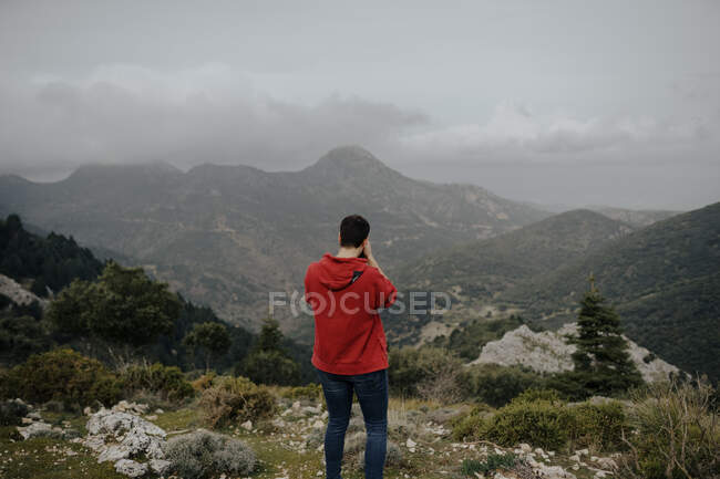Vista posterior Anónimo viajero masculino en traje casual de pie en la áspera cima de la montaña rocosa y admirar los paisajes de las tierras altas en el clima nublado en Sevilla España - foto de stock
