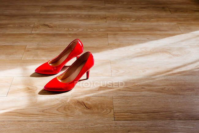 From above of pair of red shoes placed on wooden floor in sunshine — Stock Photo