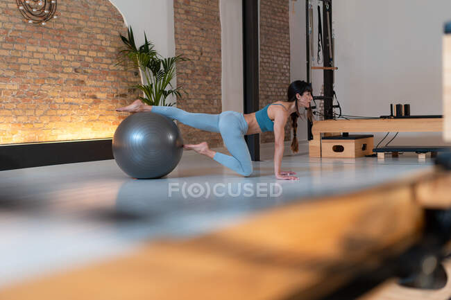 Seitenansicht einer fitten Frau in Sportbekleidung, die während des Trainings im Pilates-Studio auf einem fitten Ball trainiert — Stockfoto