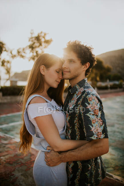 Side view young loving couple wearing casual summer clothes hugging tenderly while standing on small village street on sunny day in Greece — Stock Photo