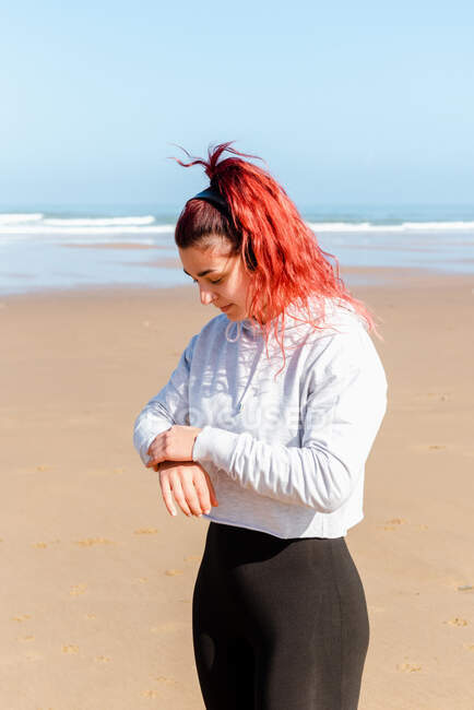 Smiling female athlete in sports clothes and headphones on ocean beach during break from workout — Stock Photo