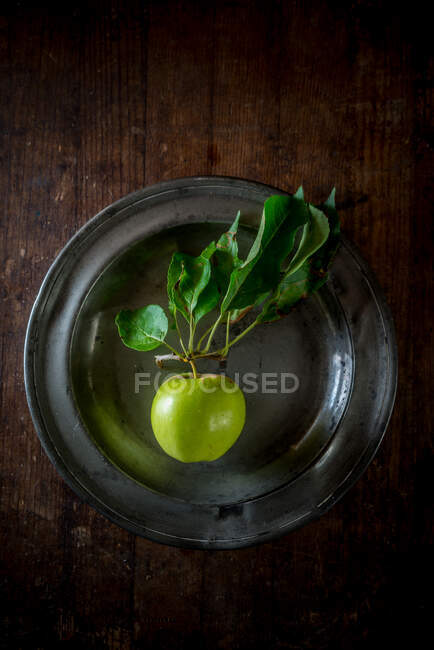 From above ripe green apple with foliage on plate on wooden table background — Stock Photo