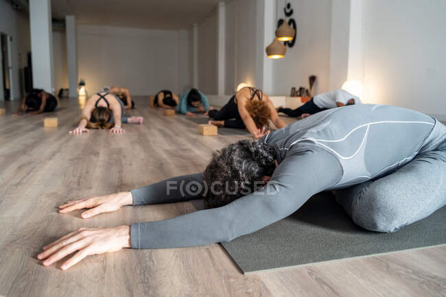 Unerkennbarer flexibler Mann praktiziert Yoga in Kapotasana, während er während des Yoga-Kurses im Studio Beine streckt — Stockfoto