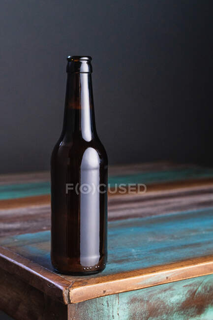 Bouteille en verre foncé de boisson alcoolisée sur une table en bois peinte en forme de carré à la maison — Photo de stock