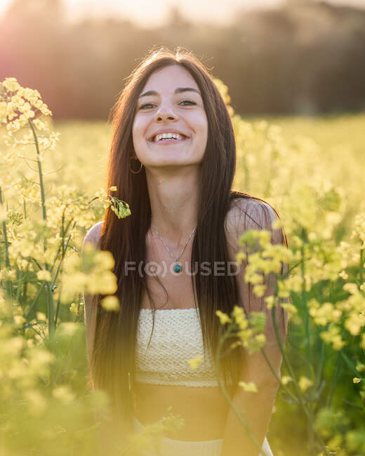 Encantada jovem morena em top branco e casaco de ganga rindo alegremente no campo de colza florescendo no dia ensolarado — Fotografia de Stock