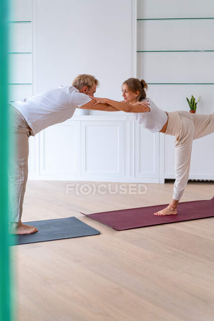 Paar in Aktivkleidung balanciert in Kriegerpose und macht Akro-Yoga, während es sich im geräumigen Raum aneinander lehnt — Stockfoto
