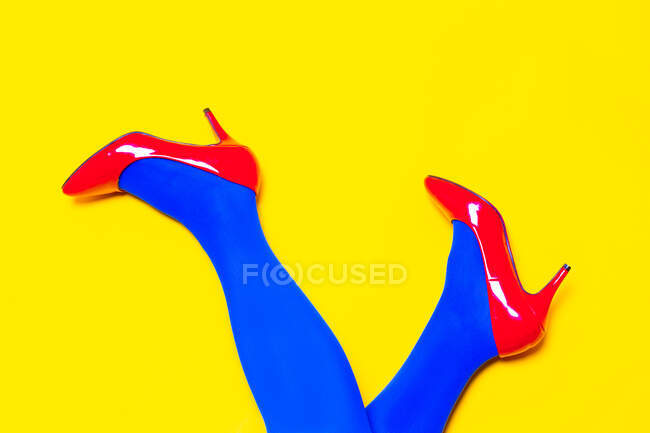 Desde arriba de la cosecha irreconocible modelo femenino con zapatos brillantes y pantimedias en estudio vívido - foto de stock
