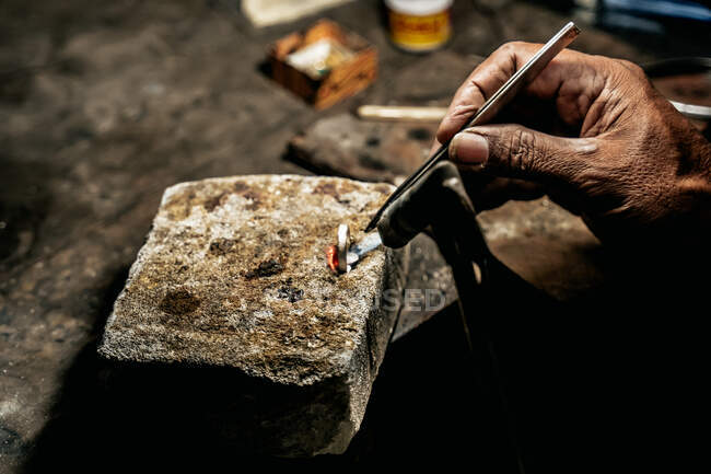 Primo piano artigiano senza volto che tiene anello d'argento su blocco di pietra e dettaglio di fusione proprio con torcia — Foto stock