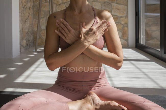 Desde arriba de la cosecha hembra concentrada irreconocible en ropa deportiva sentada con las piernas cruzadas en la esterilla de yoga en casa - foto de stock