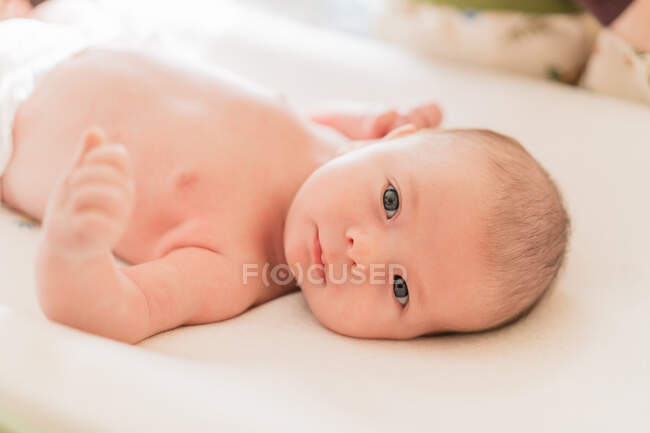 Cute little child looking at camera while lying on textile on white background — Stock Photo