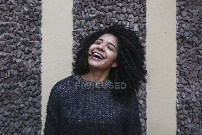 Zufriedene ethnische Frau mit Afrofrisur, die Haare wirft, während sie auf der Straße steht und lächelt — Stockfoto