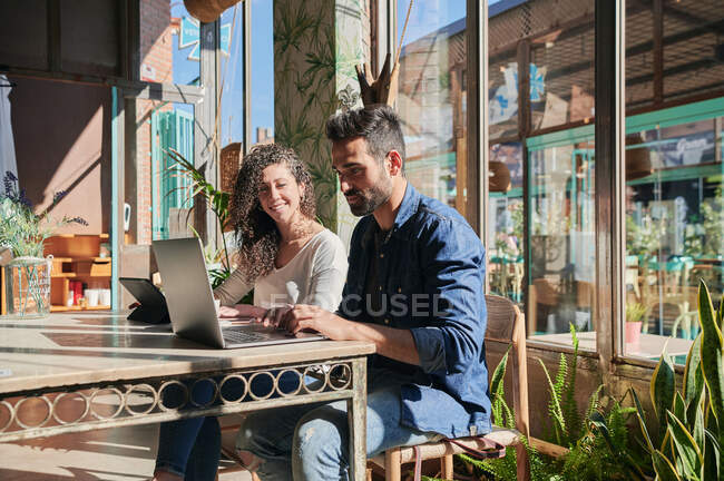 Веселі етнічні працівники, що взаємодіють за столом з нетбуком і планшетом в ресторані — стокове фото