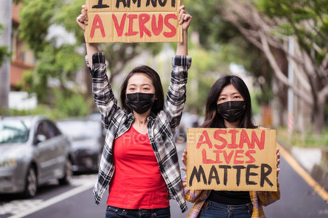 Етнічні жінки в масках, які протестують проти расизму на вулицях міста і дивляться на камеру. — стокове фото