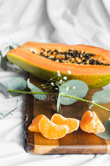 Half of pawpaw with seeds between tangerines and cumquats with leaves on white crumpled cloth — Stock Photo