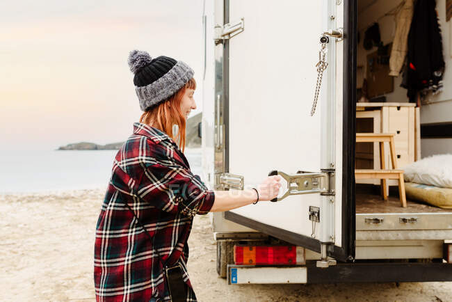 Side view of happy female hipster opening door of truck parked on beach near lake during summer trip — Stock Photo
