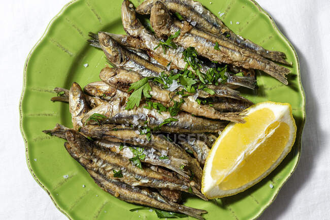 Top view plate of appetizing grilled anchovies served on table with piece of lemon and fresh herbs in restaurant — Photo de stock