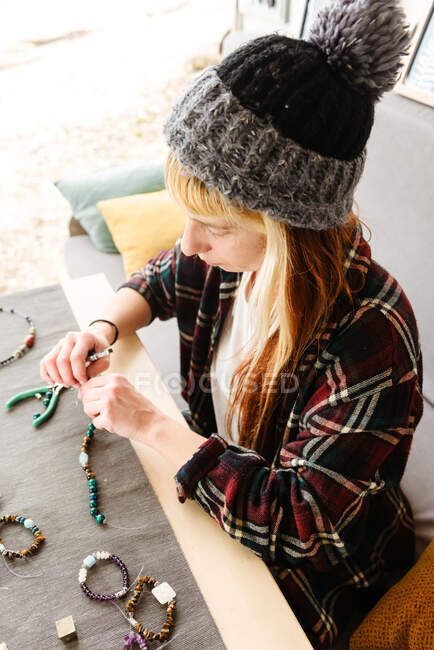 Зверху жінка-мандрівник сидить за столом у вантажівці і створює браслети ручної роботи під час подорожі — стокове фото