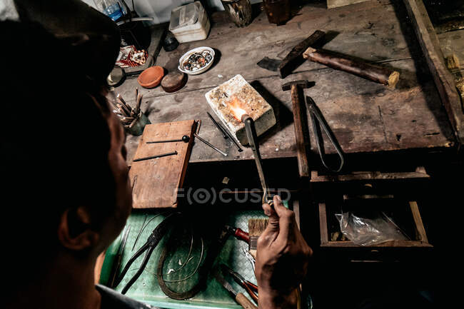 Dall'alto anonimo artigiano al banco da lavoro utilizzando torcia calda e fondendo piccoli pezzi di metallo — Foto stock