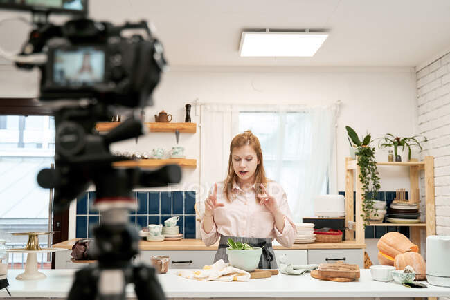 Giovane blogger donna che parla contro smartphone durante la registrazione di video culinari e guardando giù a casa — Foto stock