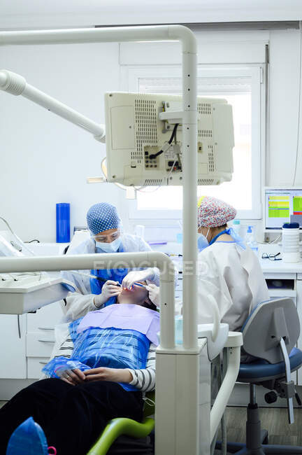 Anonymer Zahnarzt mit einem Kollegen in Uniform, der Zähne eines Patienten mit medizinischen Werkzeugen in einer modernen Klinik operiert — Stockfoto