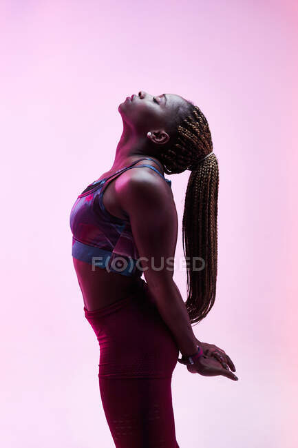 Side view of ethnic female athlete with Afro braids and clasped hands behind back training with closed eyes — Stock Photo