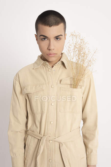 Modèle masculin androgyne en chemise tendance et avec un bouquet de plantes séchées regardant la caméra sur fond blanc en studio — Photo de stock