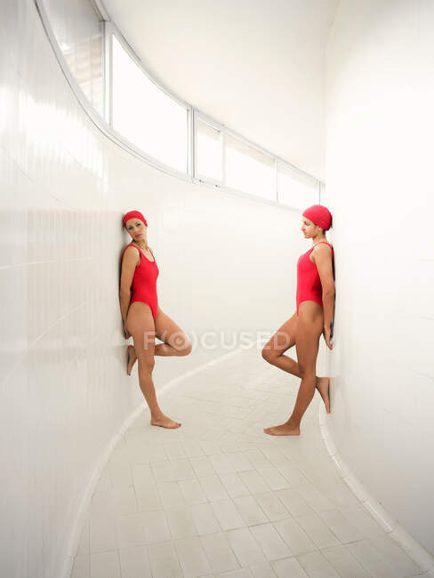 Вид сбоку на молодых спортсменок в одних и тех же купальниках с поднятыми ногами, стоящих на кафельном полу в проходе — стоковое фото