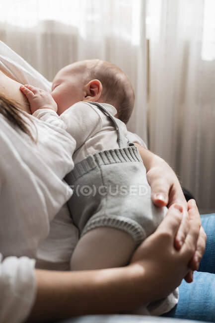 Cortado irreconhecível mãe adulta em casual desgaste chupando encantador criança enquanto sentado na sala da casa de luz — Fotografia de Stock